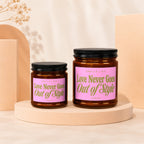 Two amber glass candles with pink labels that read "Love Never Goes Out of Style Vowed".
