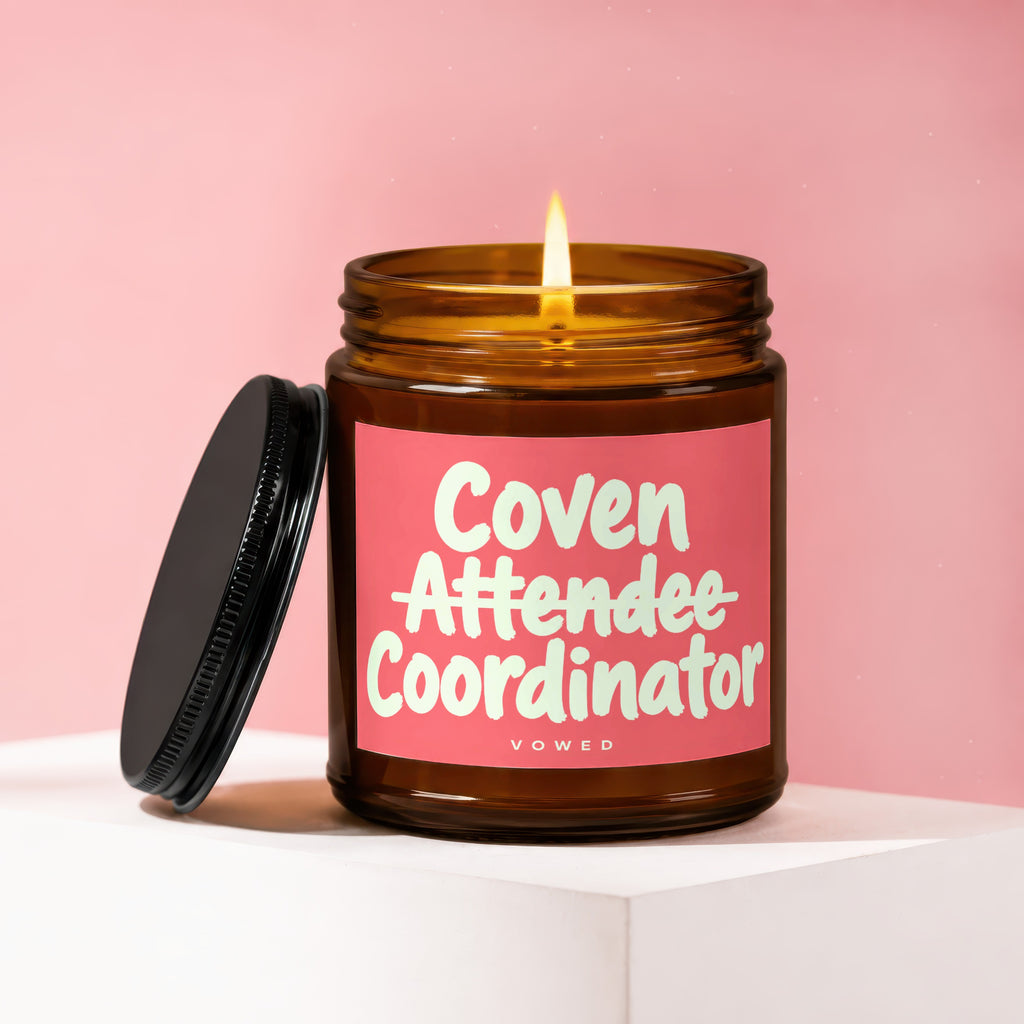 Amber jar candle with pink label reading "Coven Attendee Coordinator VOWED".