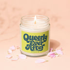 Lit candle in glass jar with "Queerly Ever After" on label, surrounded by pink petals.