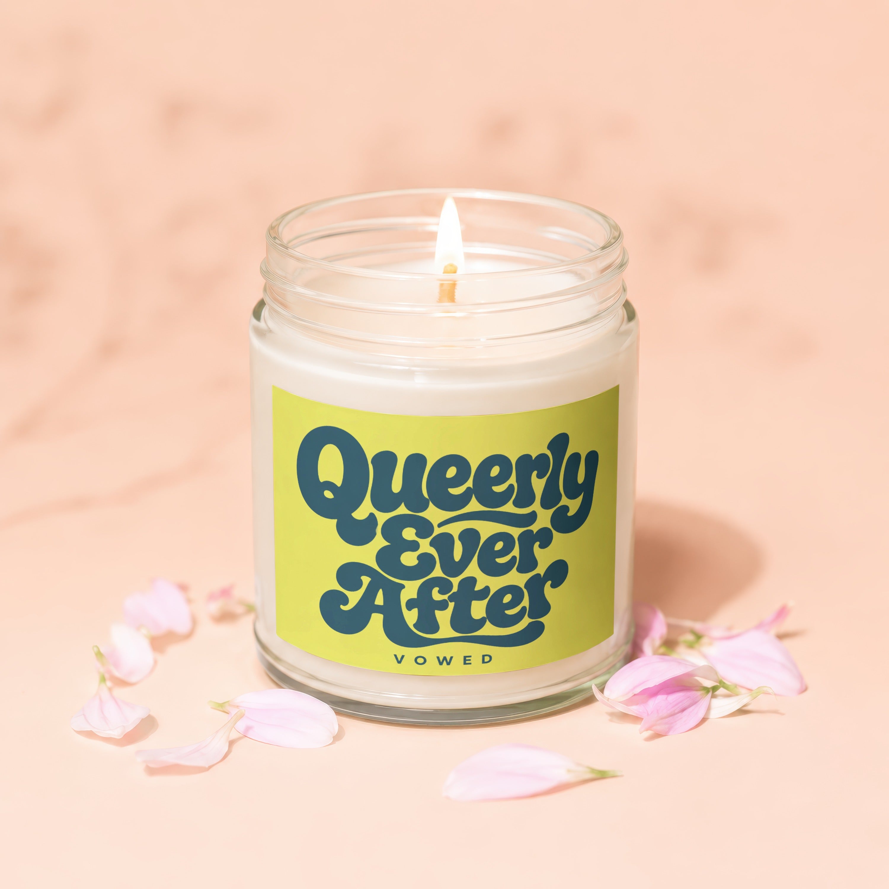 Lit candle in glass jar with "Queerly Ever After" on label, surrounded by pink petals.