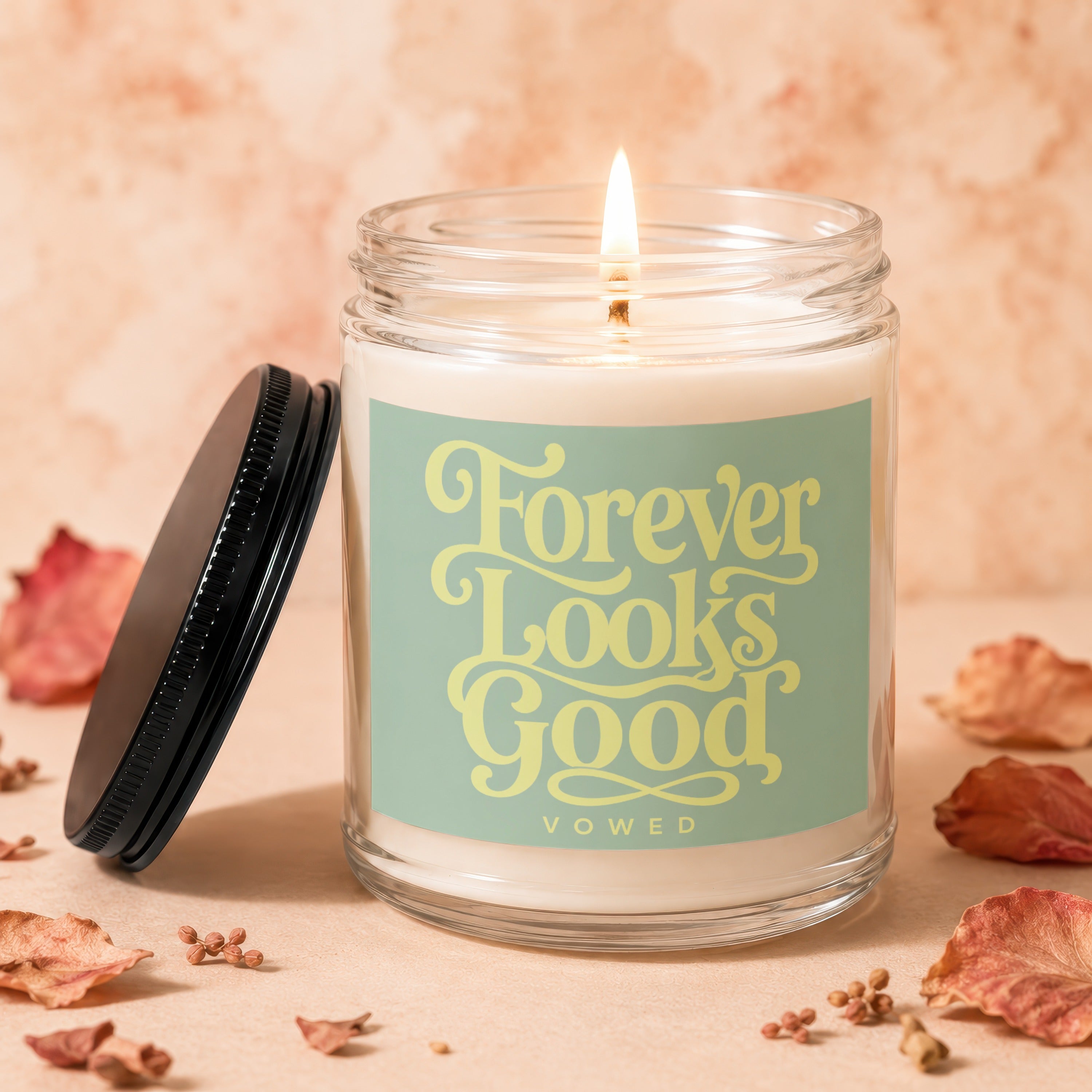 Glass candle with lit wick and label reading "Forever Looks Good"