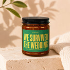 Amber jar candle with green label reading "Status: We Survived The Wedding"