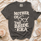 Dark grey t-shirt with cream text "Mother of the Bride Era" and heart-shaped glasses.