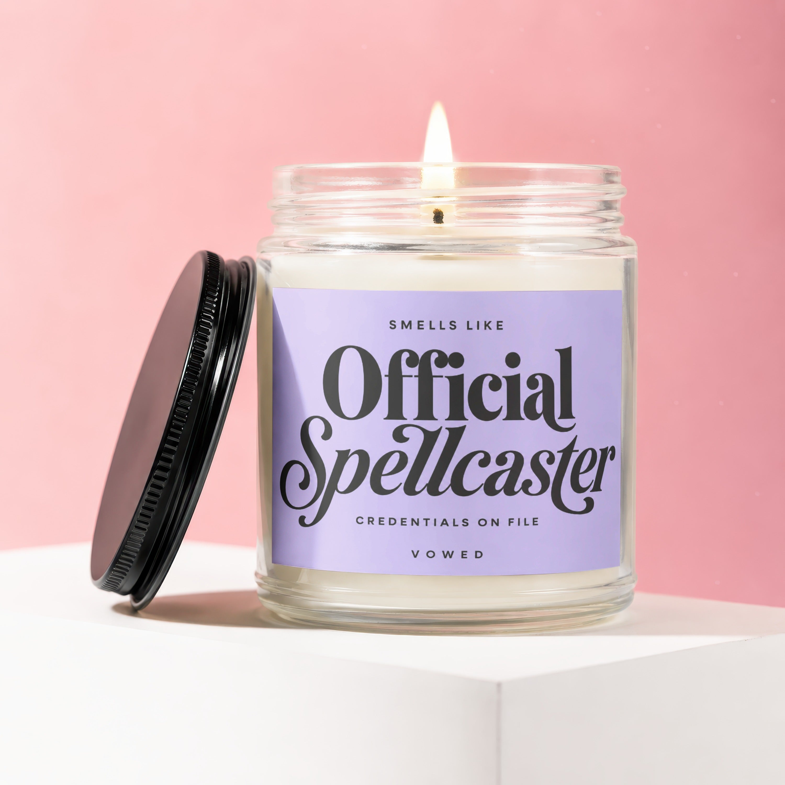 Lit jar candle with purple label reading "Smells Like Official Spellcaster".