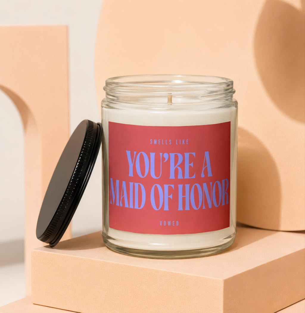 Glass candle with red label reading "Smells like You're a Maid of Honor"