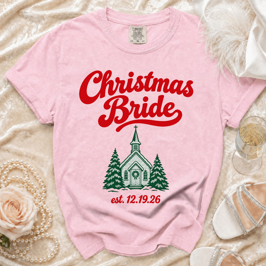 A pink Comfort Colors t-shirt with red text reading Christmas Bride above a green church graphic and the date 12.19.26.