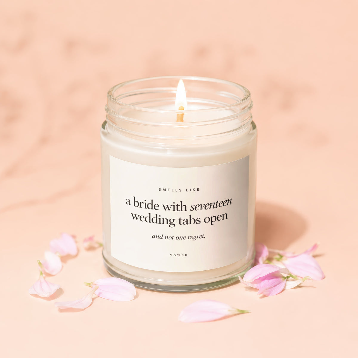 Lit candle in a jar with a label reading "Smells like a bride with seventeen wedding tabs open and not one regret. Vowed."