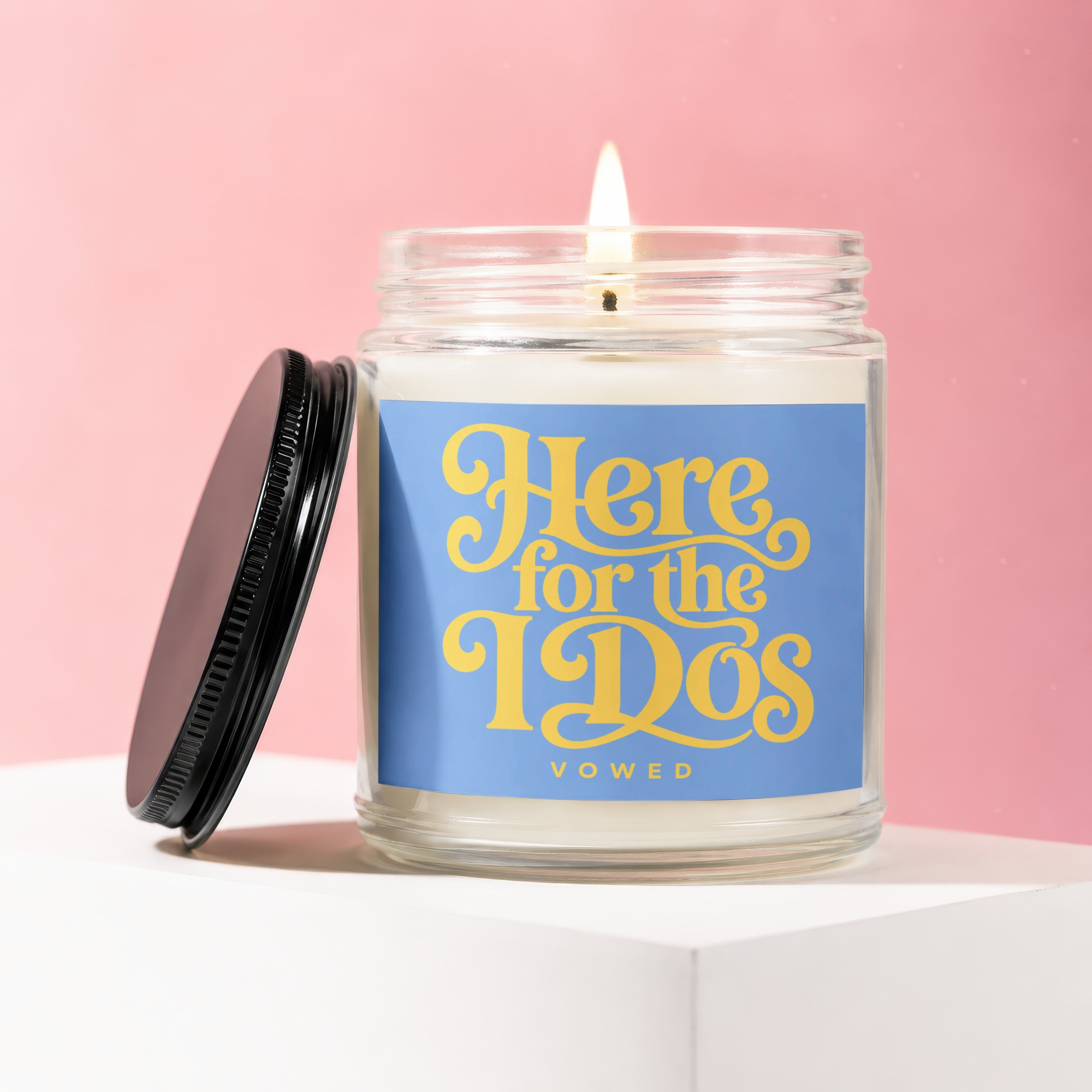 Scented candle with lit wick, blue label reading "Here for the IDs" and "VOWED".