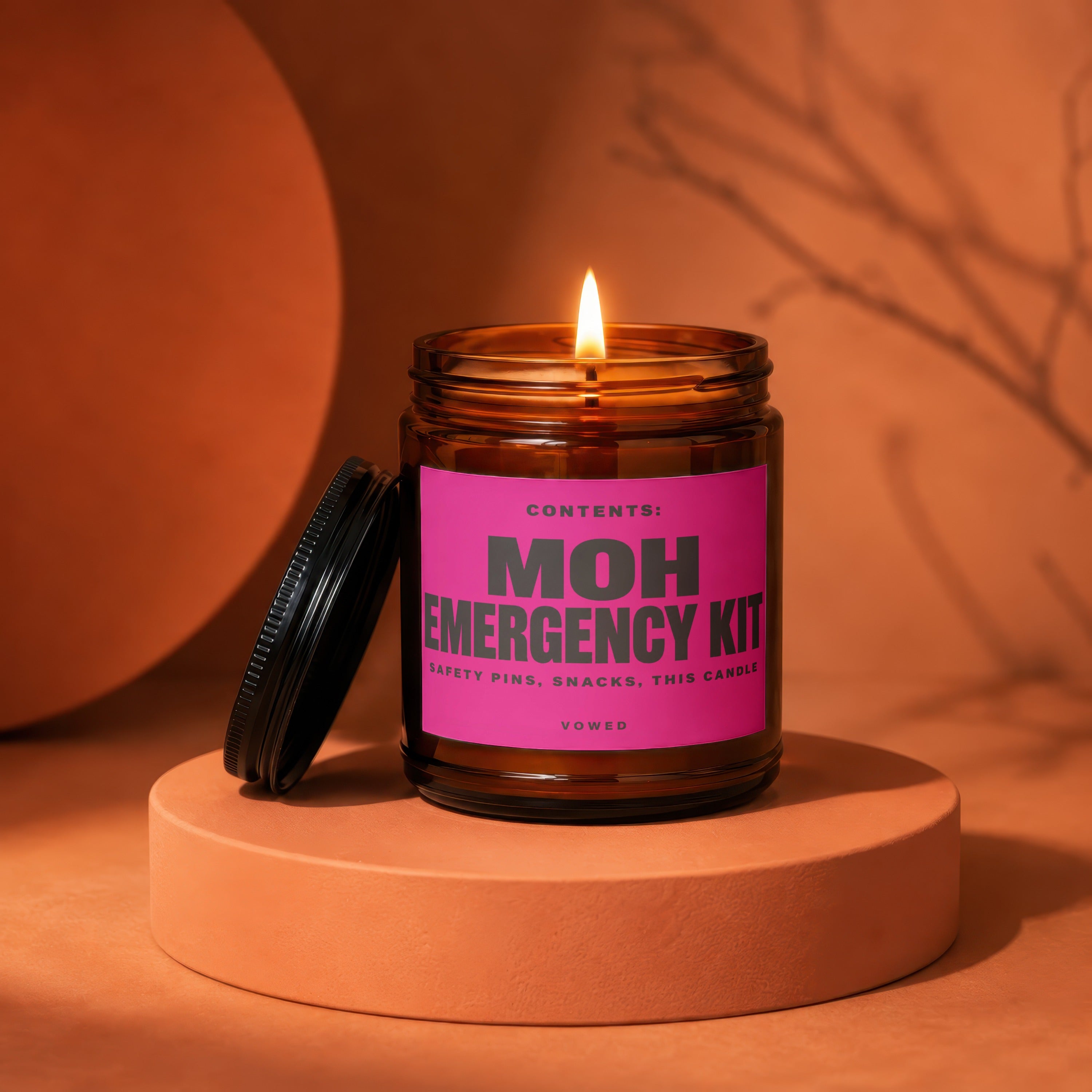 Amber jar candle with lit wick and pink label reading "MOH EMERGENCY KIT"