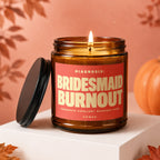 Amber glass candle with lit wick, lid off, and "Bridesmaid Burnout" label.