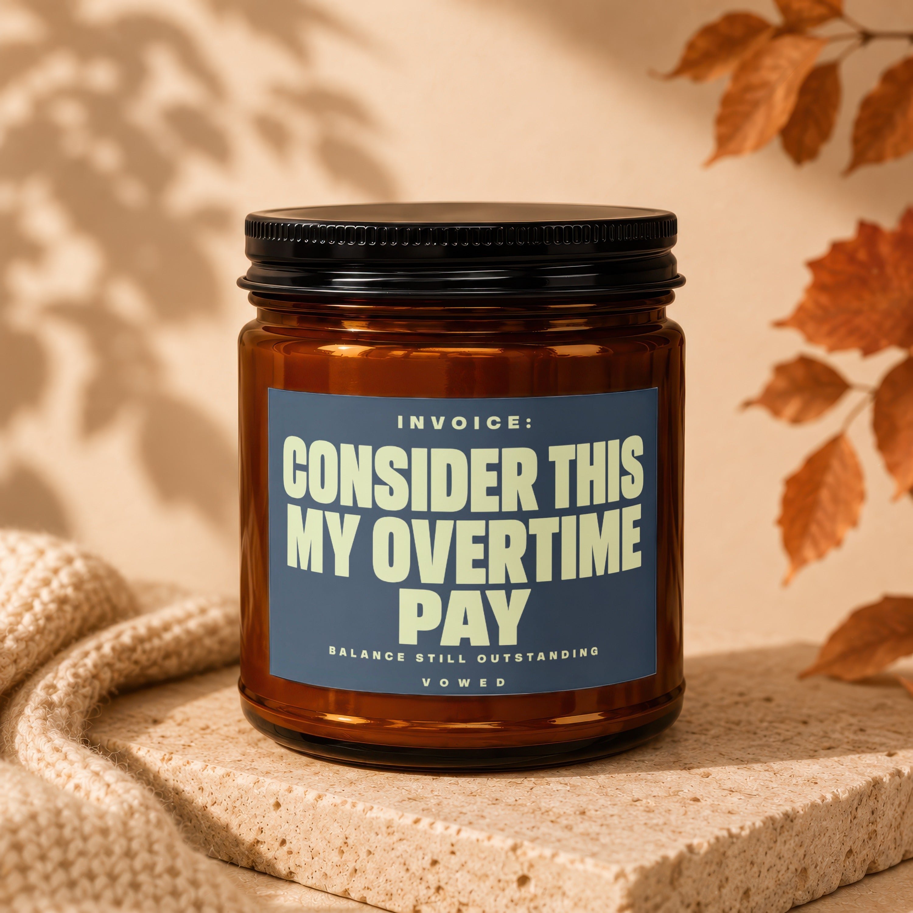 Amber jar candle with label reading "INVOICE: CONSIDER THIS MY OVERTIME PAY BALANCE STILL OUTSTANDING VOWED".