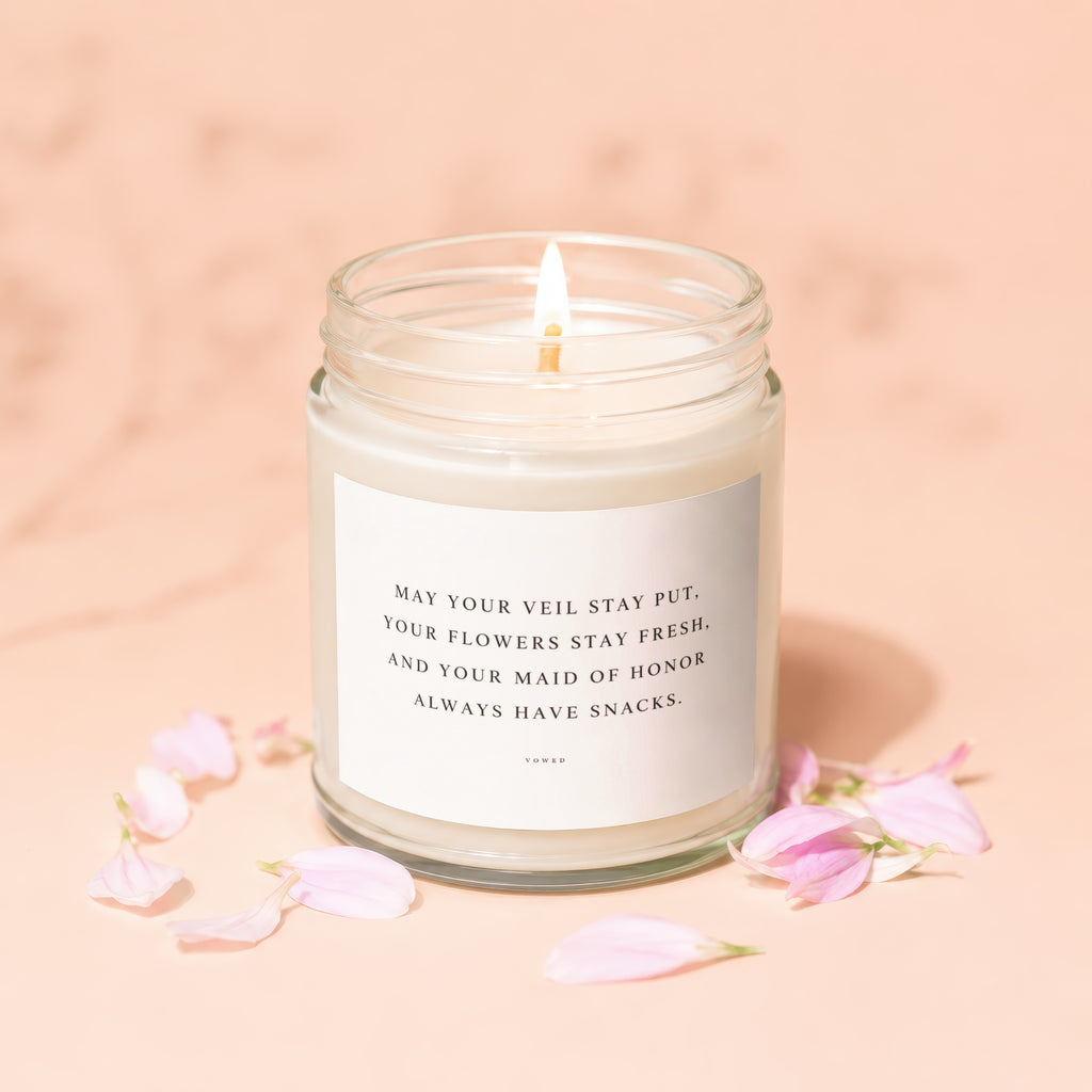Glass candle with text "May your veil stay put, your flowers stay fresh, and your maid of honor always have snacks" surrounded by petals.