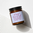 Glass candle jar with black lid and label reading "Our first of many VOWED".