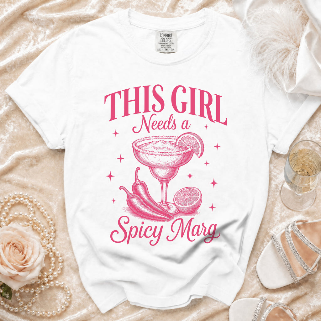 White t-shirt with pink graphic text "This Girl Needs a Spicy Marg" and margarita illustration.