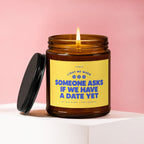 Amber candle with lit wick and black lid, text reads "Light me when someone asks if we have a date yet".