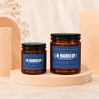 Two amber glass candles with dark lids. Labels read "HE MARRIED UP."