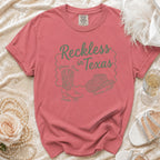 Coral t-shirt with "Reckless in Texas" design featuring cowboy boots and hat.