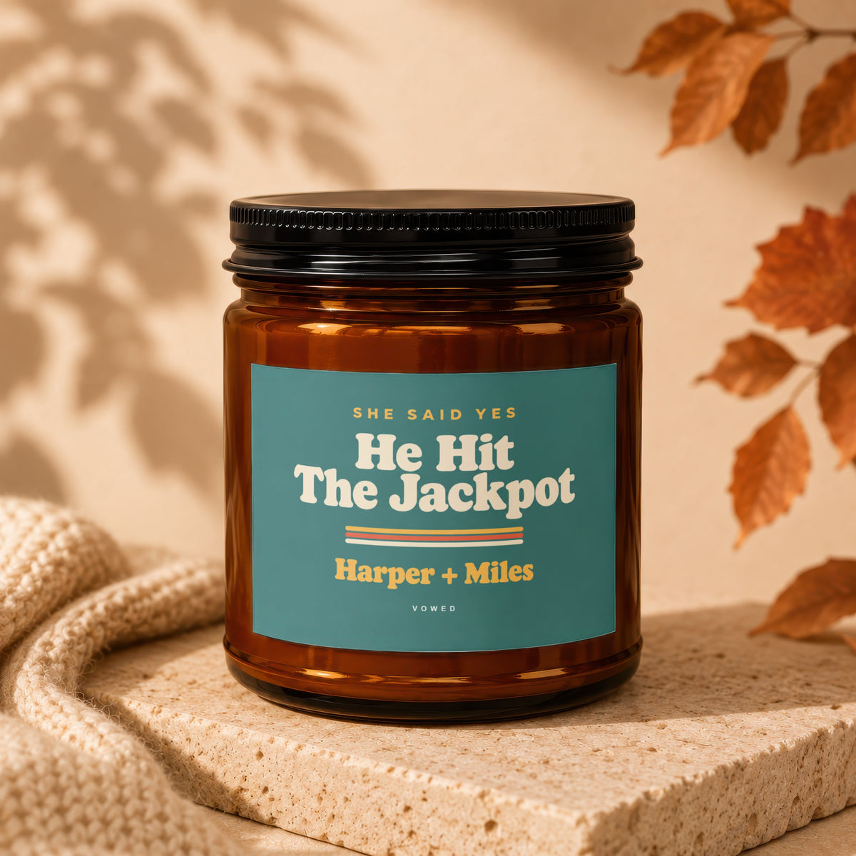Amber candle with teal label reading "He Hit The Jackpot Harper + Miles".