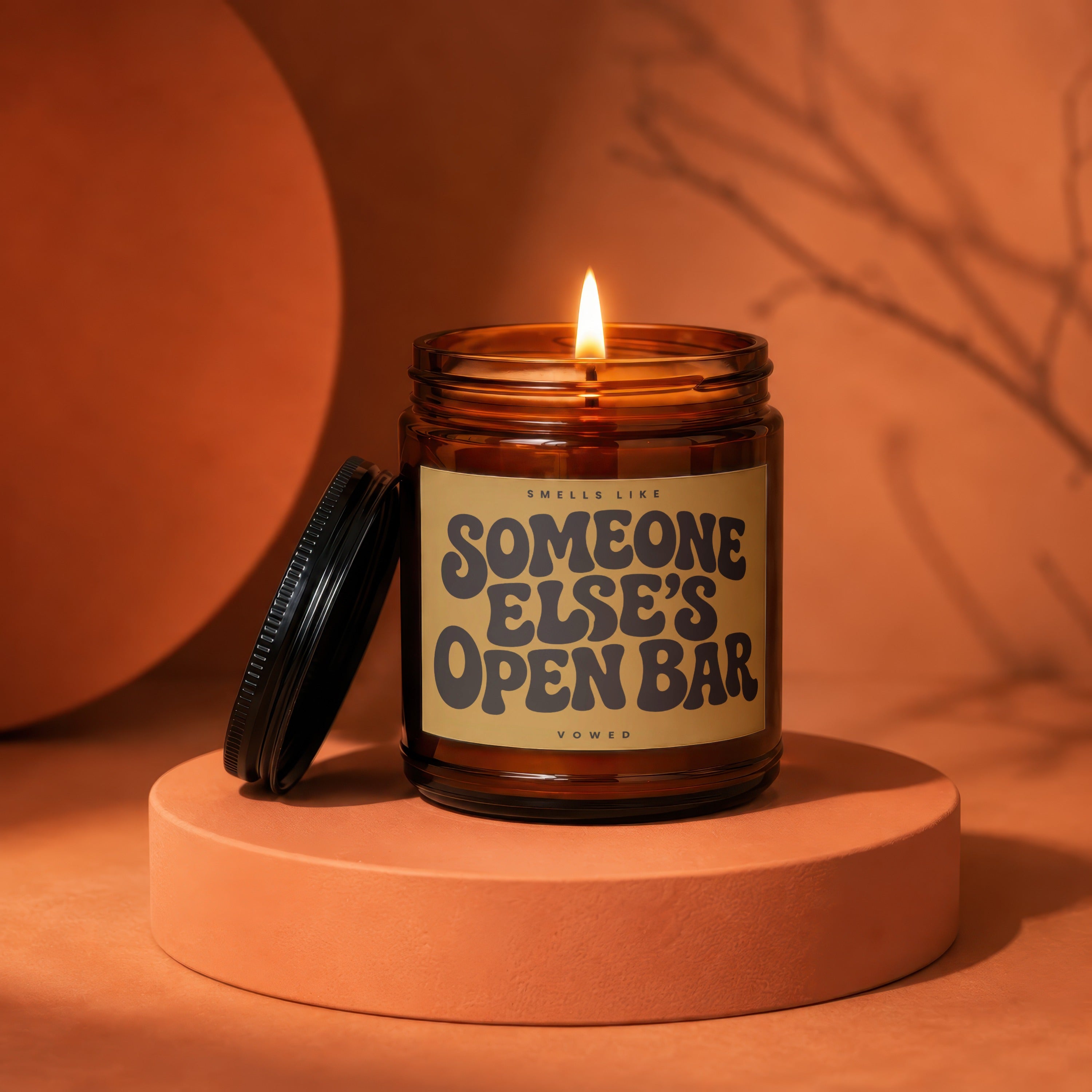 Amber jar candle with lit flame, label reads "Smells Like Someone Else's Open Bar".