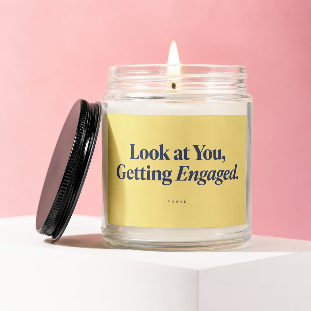 Glass candle with yellow label reading "Look at You, Getting Engaged. VOWED".