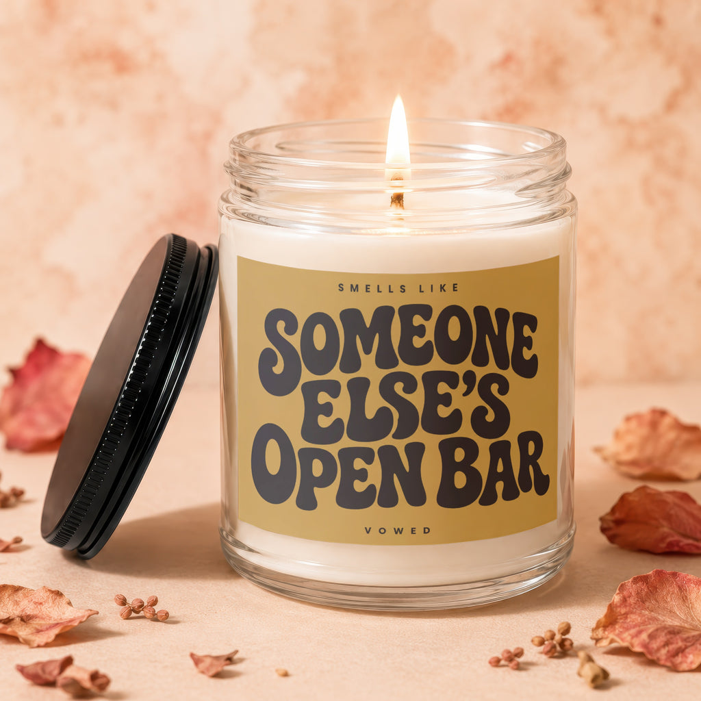 Glass jar candle with lit wick, reads "Smells Like Someone Else's Open Bar".