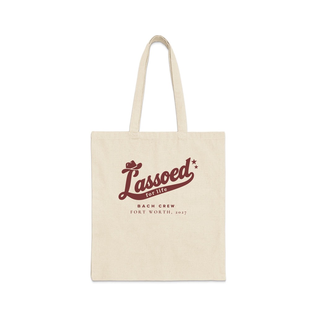 A beige canvas tote bag features brown text reading "Lassoed for life Bach Crew Fort Worth, 2027".