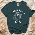 Teal t-shirt with white graphic of ghost bride holding martini and text "Spooky Bride's Club".