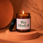 Brown glass candle with a lit wick and label "We Made It".