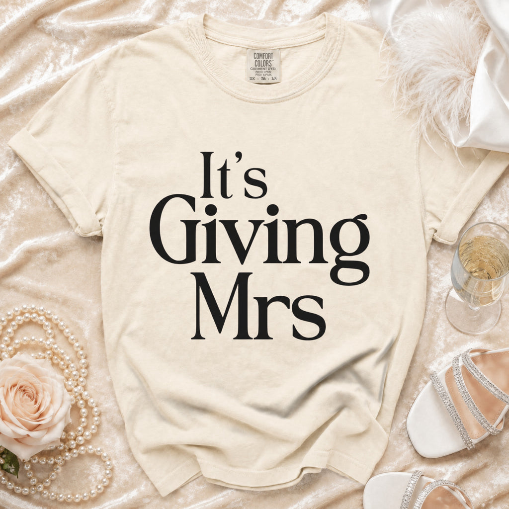 Cream t-shirt with black text "It's Giving Mrs" and Comfort Colors tag.
