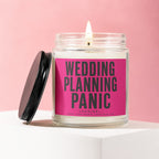 Glass candle with lit wick, black lid nearby, pink label reads "Wedding Planning Panic".