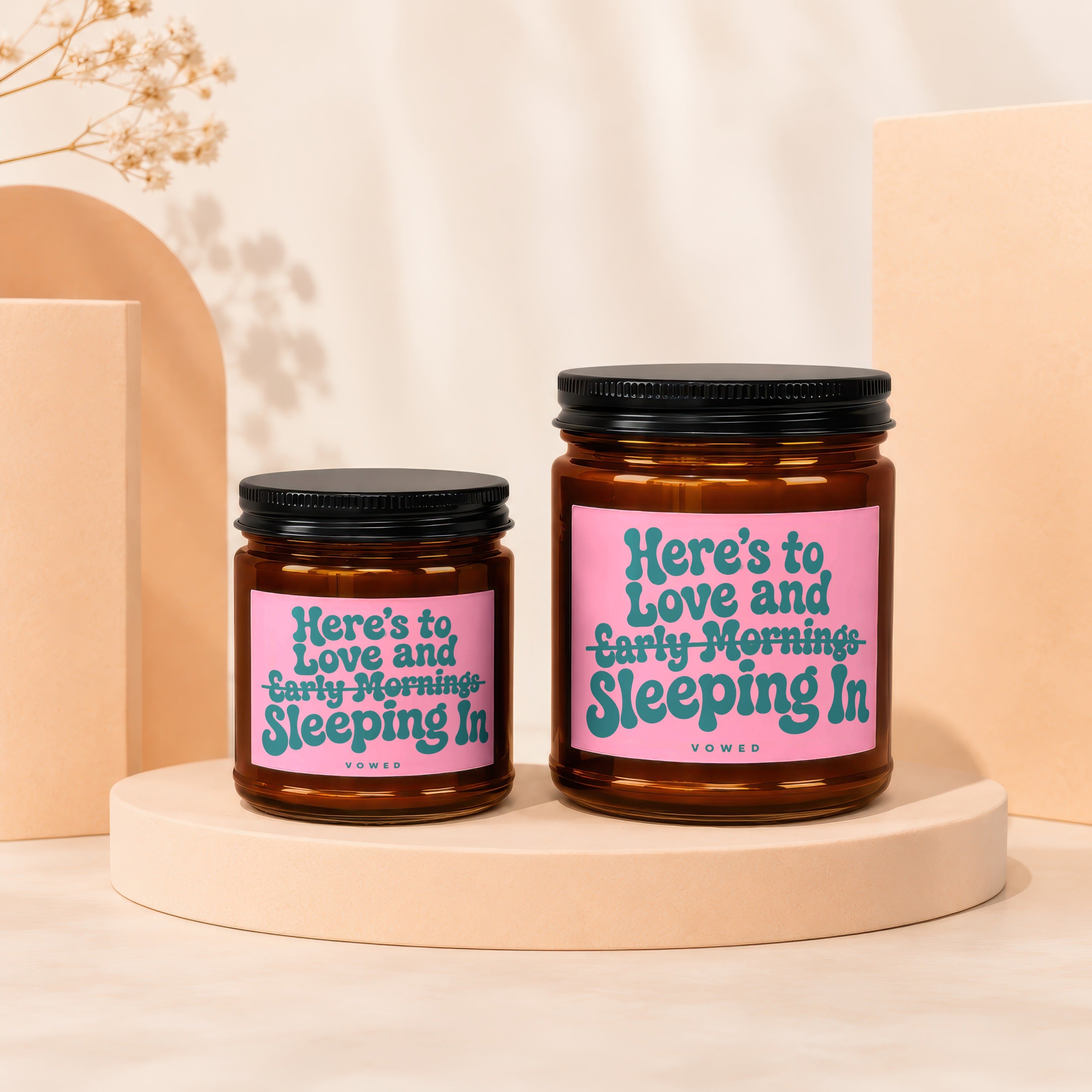 Two amber glass candles with black lids and pink labels featuring teal text.
