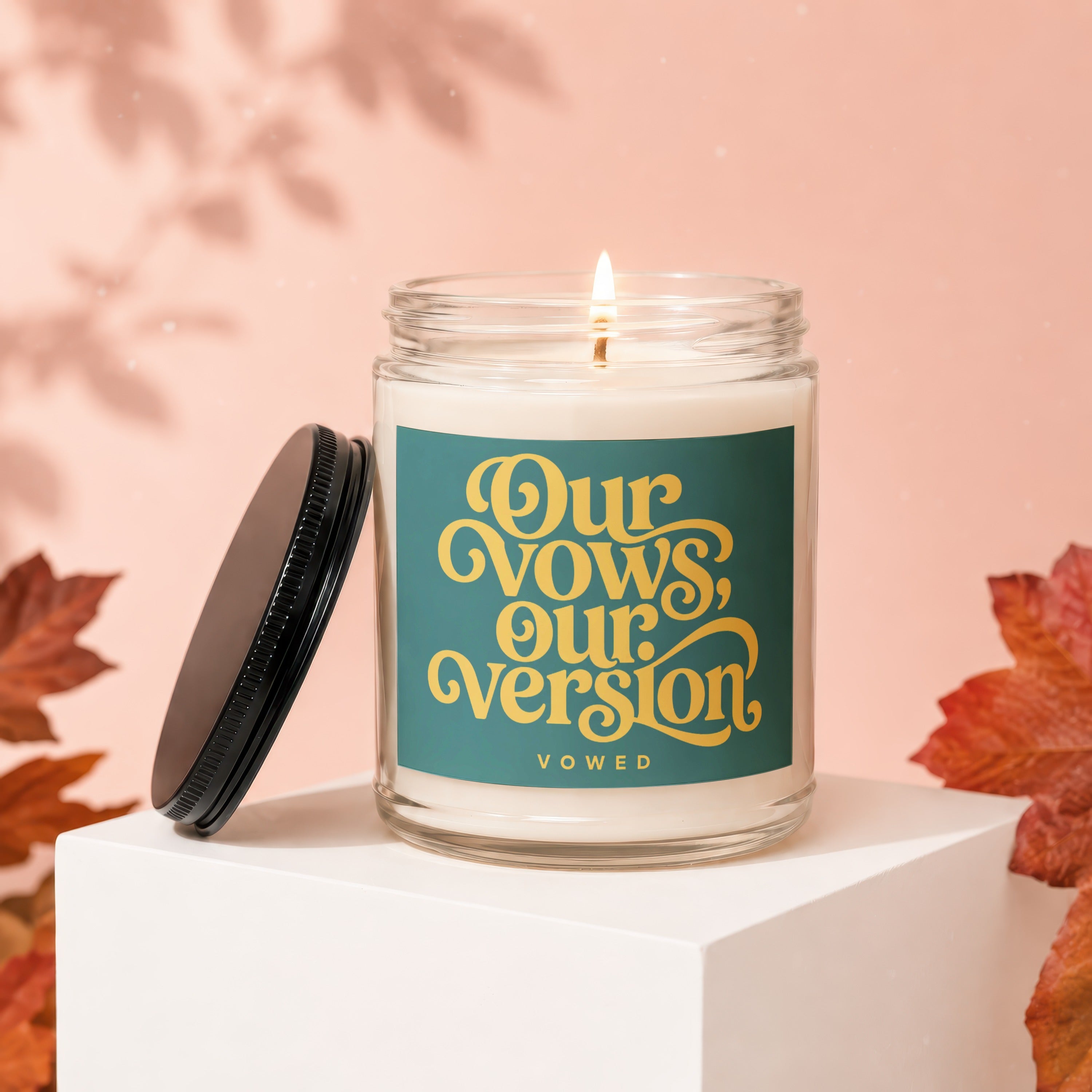 Candle with "Our Vows, Our Version, VOWED" text on teal label, lit flame.