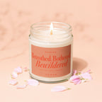 Glass jar candle with lit wick and text: Warning: Betrothed, Bothered, Bewildered, Vowed.
