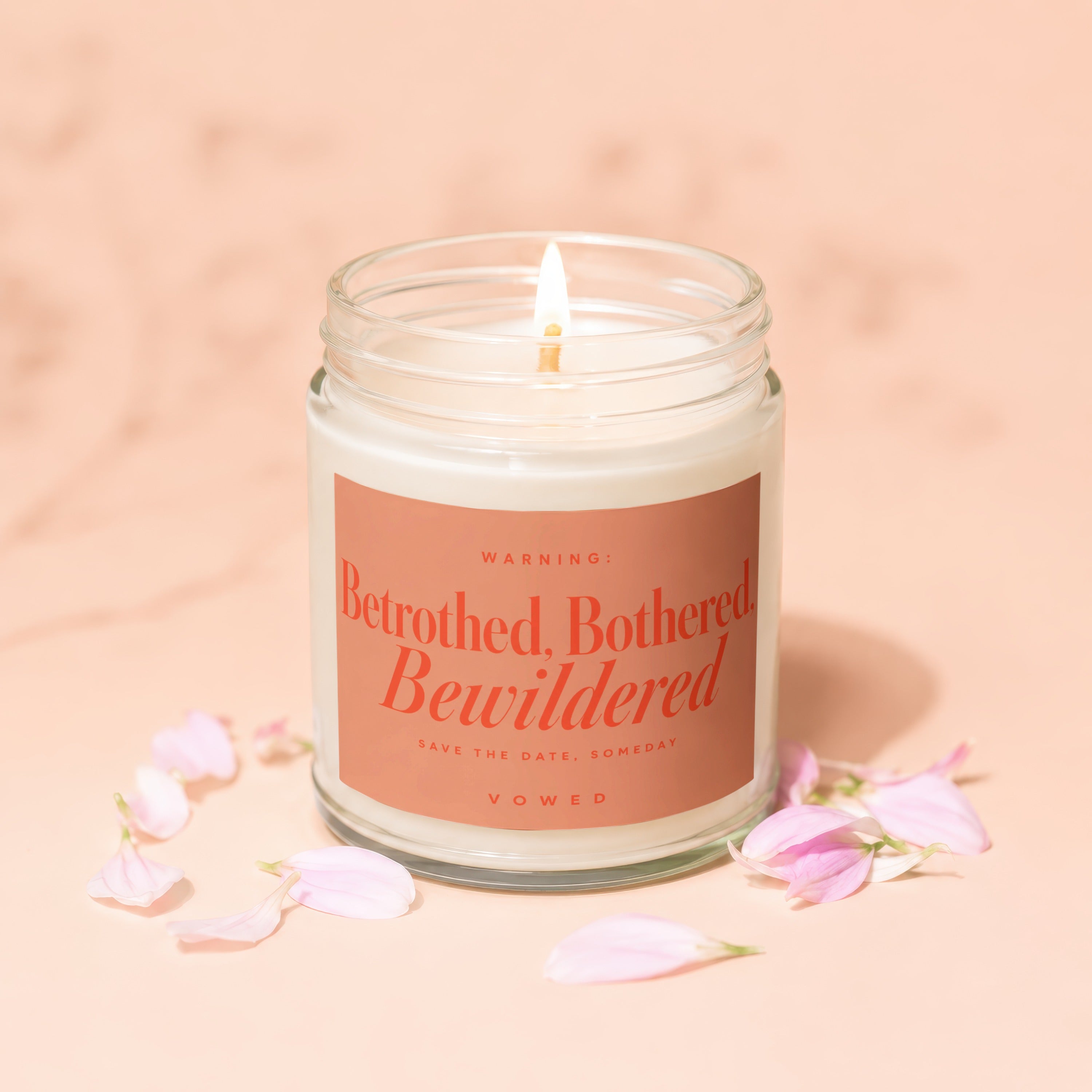 Glass jar candle with lit wick and text: Warning: Betrothed, Bothered, Bewildered, Vowed.