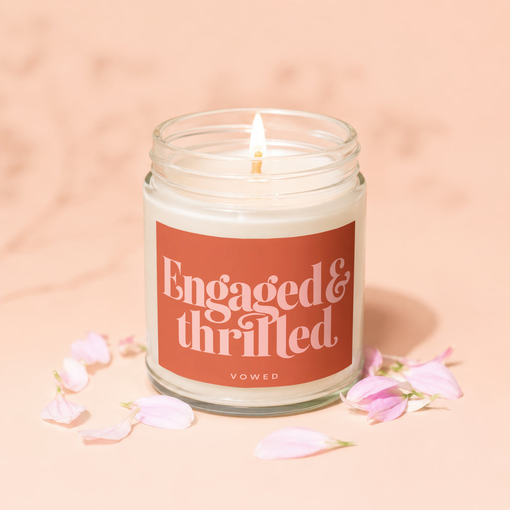 Candle with "Engaged & thrilled" text, surrounded by pink petals.