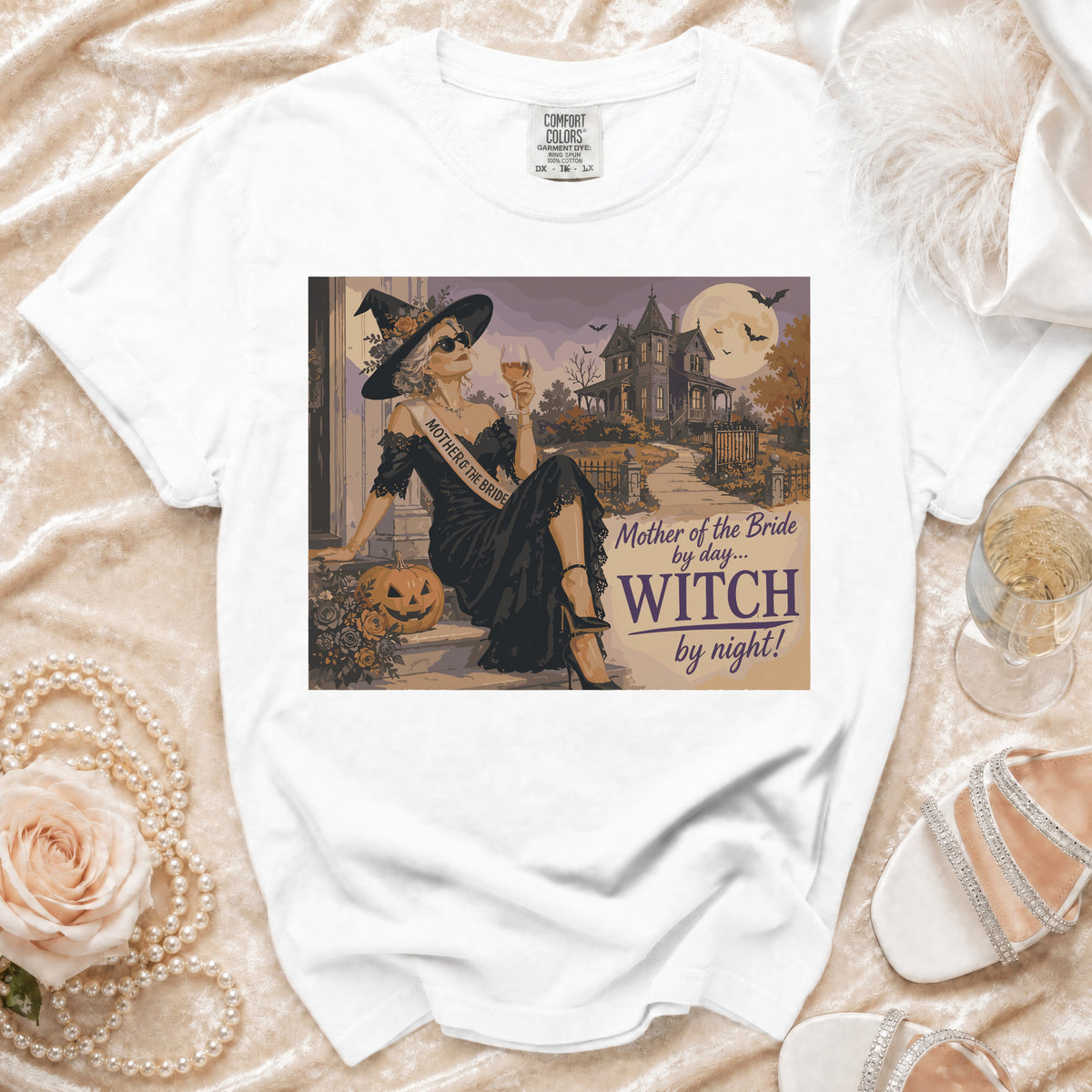 White t-shirt graphic with a witch and spooky mansion, text reads "Mother of the Bride by day... WITCH by night!".