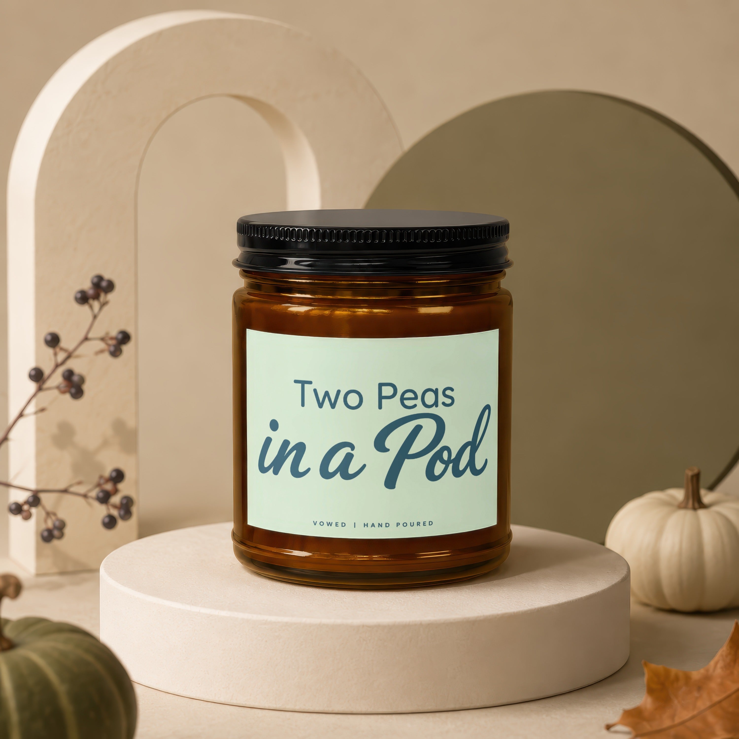 Glass candle labeled 'Two Peas in a Pod' with decorative pumpkins and fall foliage.