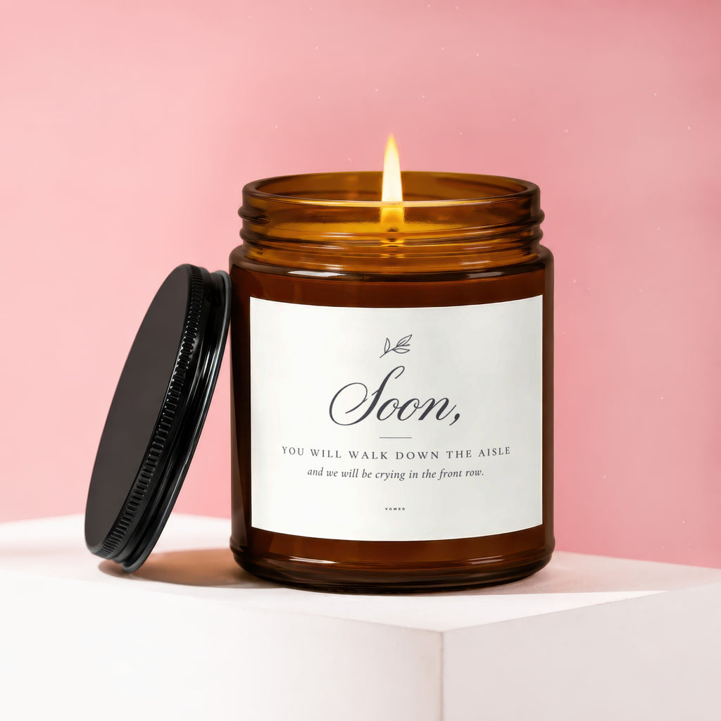 Amber jar candle with burning wick and label: "Soon, You will walk down the aisle and we will be crying in the front row."