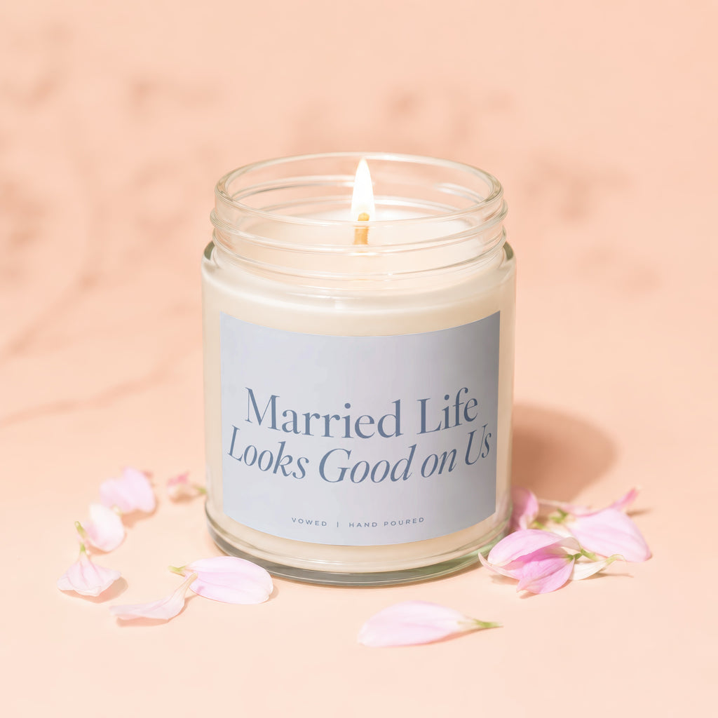 Lit candle in glass jar with label "Married Life Looks Good on Us", surrounded by pink petals.