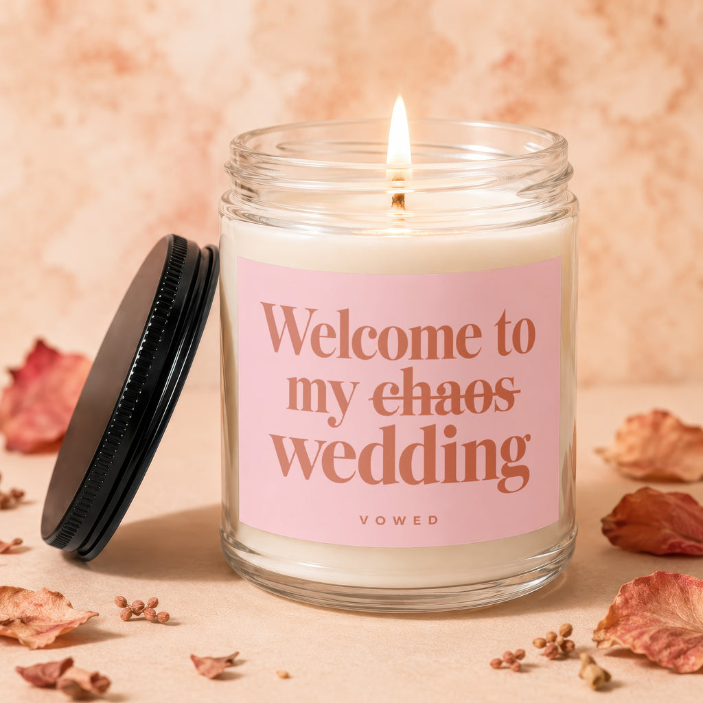 Candle with pink label reading "Welcome to my chaos wedding," VOWED, on a light peach background.