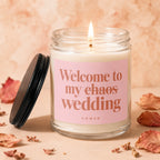 Candle with pink label reading "Welcome to my chaos wedding," VOWED, on a light peach background.