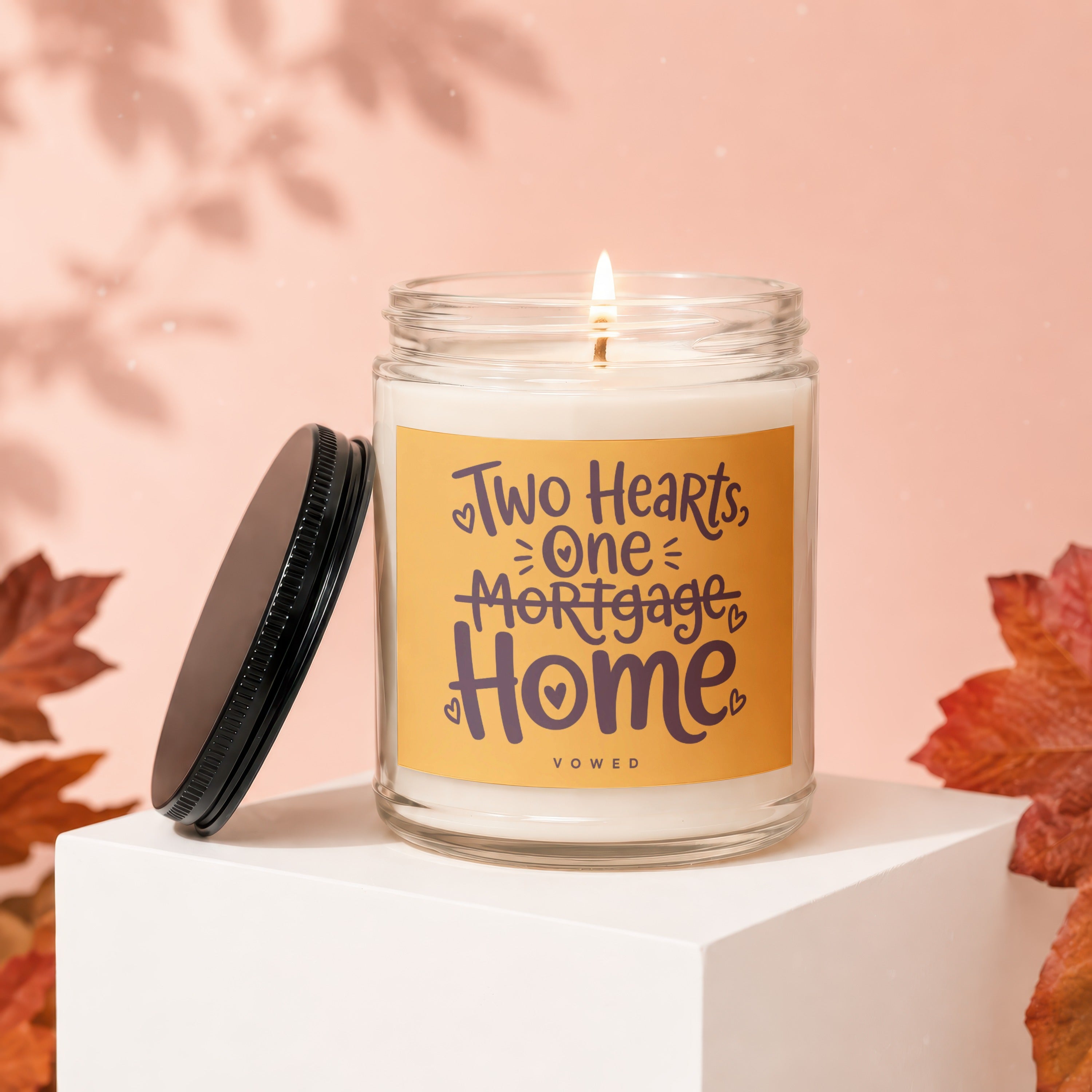 Glass jar candle with "Two Hearts, One Mortgage, Home" text and a lit wick.