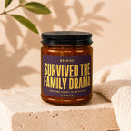 Amber jar candle with label "WARNING: SURVIVED THE FAMILY DRAMA SEATING CHART CLASSIFIED VOWED".