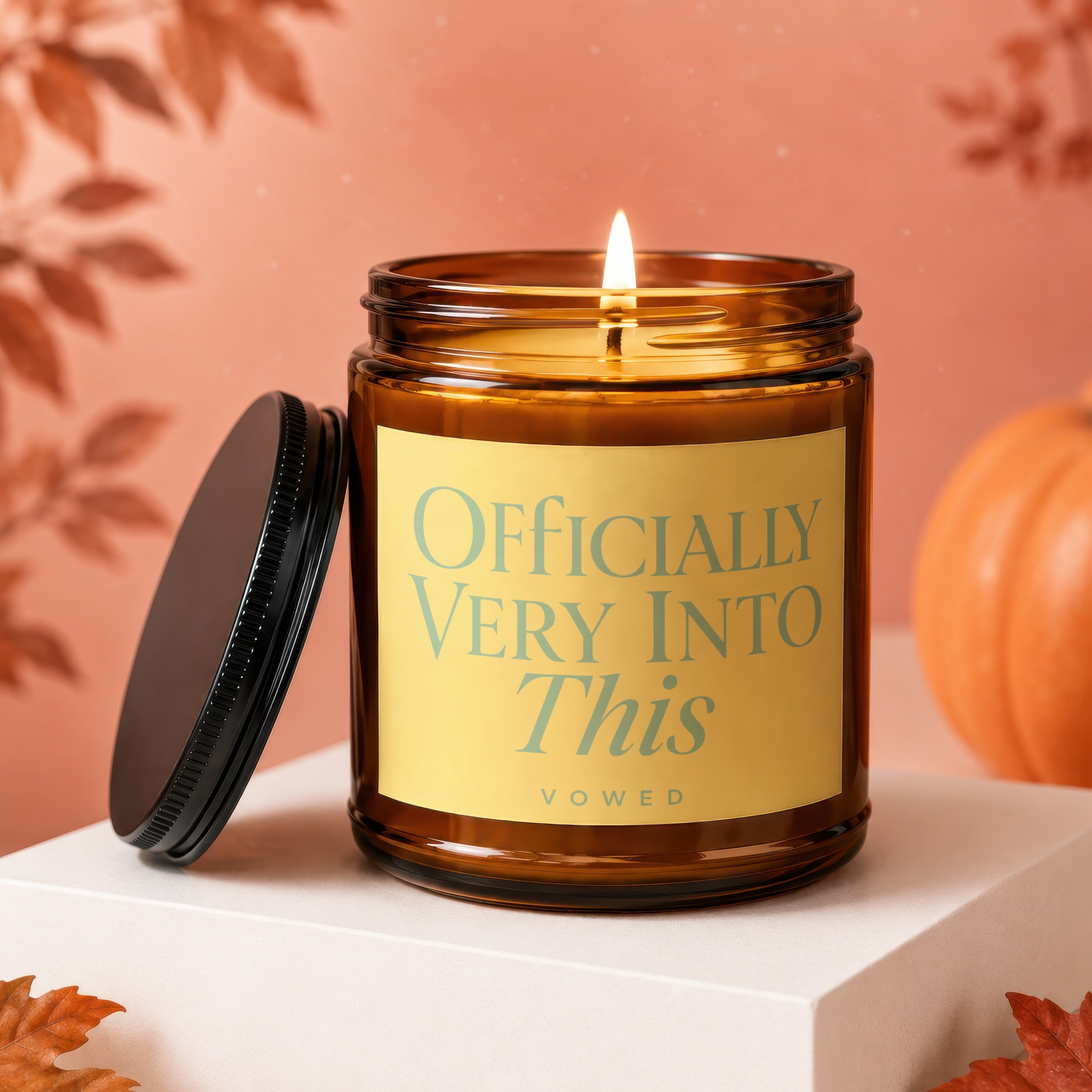 Amber candle with lit flame, "Officially Very Into This" text, and a black lid.