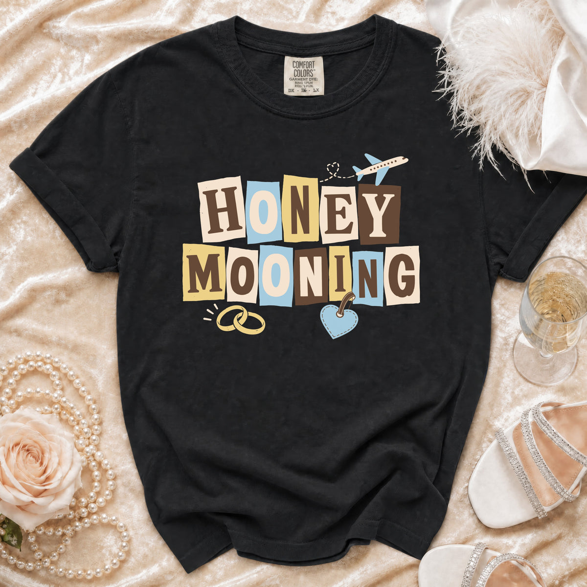Black t-shirt with "HONEYMOONING" text, wedding rings, and airplane graphic.