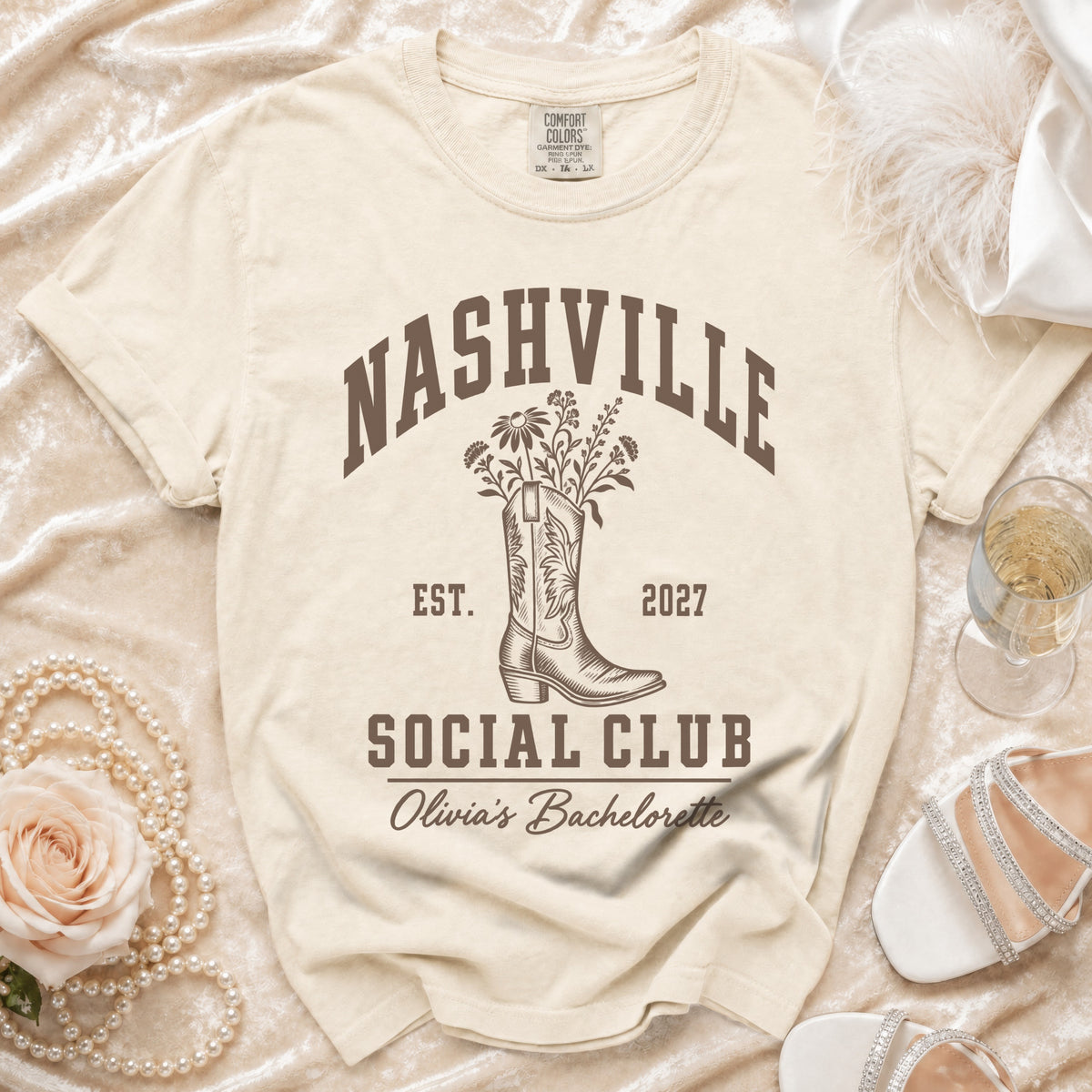 Cream t-shirt featuring brown text reading Nashville Social Club, a cowboy boot, flowers, and Olivia's Bachelorette.