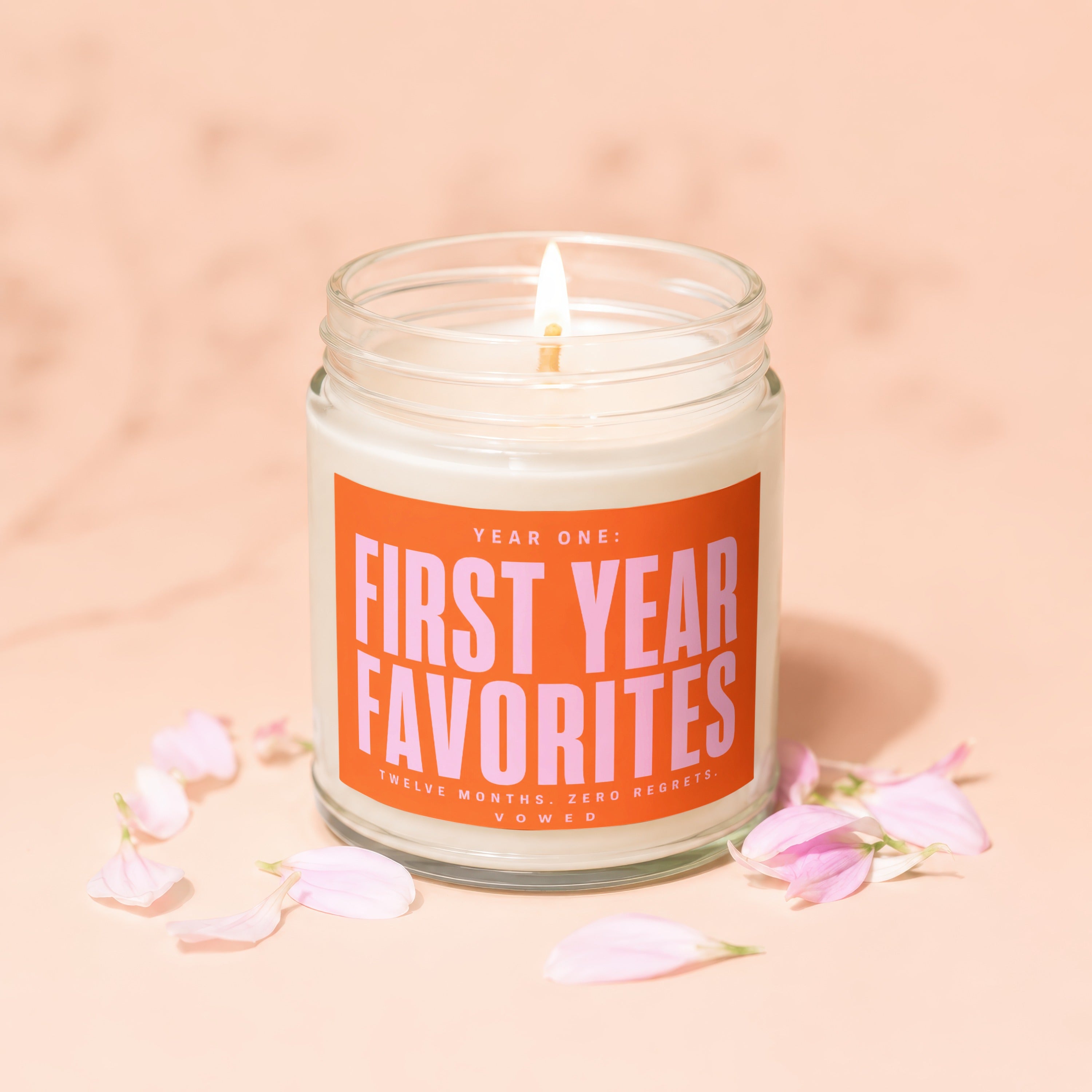 Jar candle with an orange label reading "FIRST YEAR FAVORITES" surrounded by pink petals.