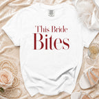 White t-shirt with "This Bride Bites" text in burgundy, styled with pearls, rose, and champagne.
