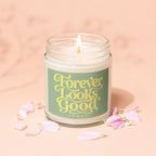 Lit candle with "Forever Looks Good" text on label, surrounded by pink flower petals.