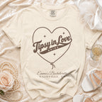 Cream t-shirt featuring a rope heart graphic, the text "Tipsy in Love Bride," and personalized bachelorette details.